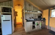 Luxury safari tent kitchen in the Netherlands with fridge, microwave, utensils, and dishwasher.