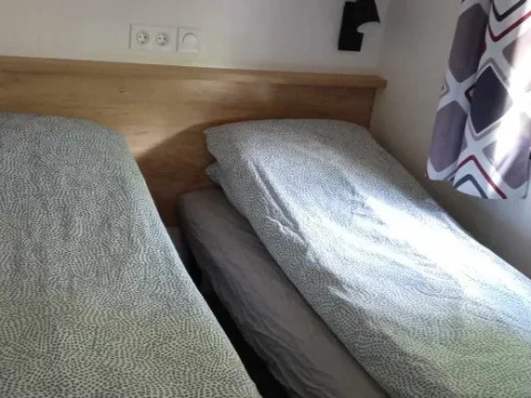 Twee enkele bedden met grijs beddengoed in een heldere kamer bij Luxe Premium Lodge + jacuzzi, Flower Camping de la Trye.