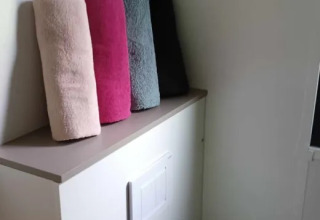 Vier opgerolde handdoeken in verschillende kleuren op een kast in Luxe Premium Lodge bij Flower Camping de la Trye.