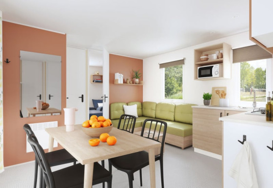 Soggiorno moderno di Cordelia Lodges con divano verde, tavolo da pranzo, cucina e vista sulla natura.