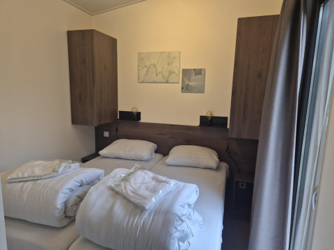 Soveværelse i 'Cube' Lodge 4 ved De Utrechtse Heuvelrug, Holland, med to senge, hvidt sengetøj og træskabe.