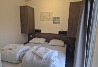 Soveværelse i 'Cube' Lodge 4 ved De Utrechtse Heuvelrug, Holland, med to senge, hvidt sengetøj og træskabe.