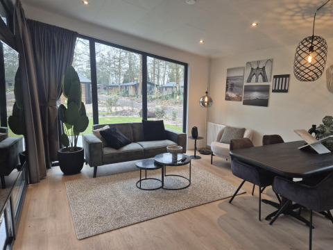 Moderne stue i Cube Lodge 4, De Utrechtse Heuvelrug, med store vinduer, sofa og spisebord.