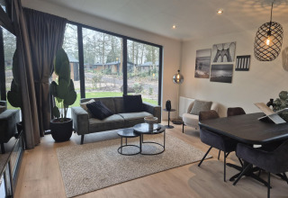 Moderne stue i Cube Lodge 4, De Utrechtse Heuvelrug, med store vinduer, sofa og spisebord.