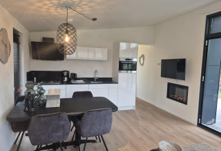 Moderne lodgekøkken og spisestue med sort bord, elegante stole og pejs i De Utrechtse Heuvelrug, Holland.