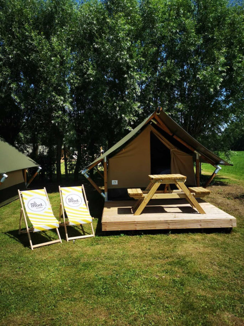 Safaritent op een houten terras met picknicktafel en twee ligstoelen, omgeven door gras en bomen.