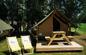 Safari tent with a wooden deck, picnic table, and two lounge chairs, set in green grass and trees.