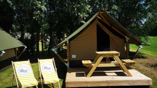 Safaritent op een houten terras met picknicktafel en twee ligstoelen, omgeven door gras en bomen.