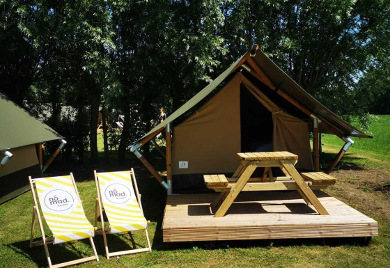 Safaritent op een houten terras met picknicktafel en twee ligstoelen, omgeven door gras en bomen.