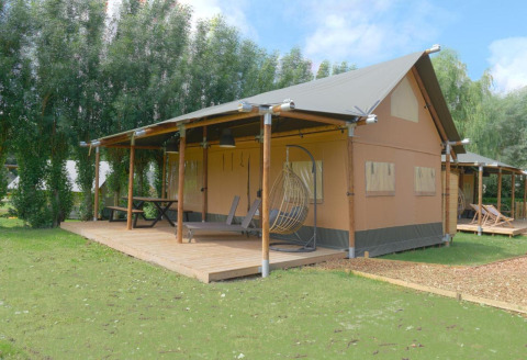 Nomad Family safaritent met ruim houten terras, hangstoel en picknicktafel in een groene omgeving.