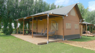 Nomad Family safaritent met ruim houten terras, hangstoel en picknicktafel in een groene omgeving.