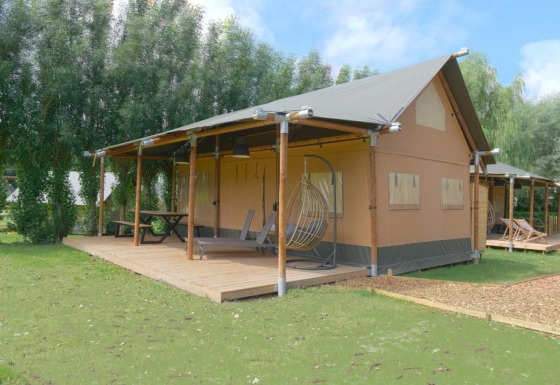 Nomad Family safaritent met ruim houten terras, hangstoel en picknicktafel in een groene omgeving.