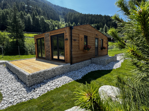 Cabane en bois avec terrasse au Camping Arlberg en Autriche, entourée de collines verdoyantes et d’arbres.
