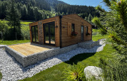 Cabane en bois avec terrasse au Camping Arlberg en Autriche, entourée de collines verdoyantes et d’arbres.