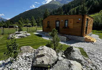 Cabaña Arlberg en Austriaparks Camping Arlberg, Austria, rodeada de césped verde, piedras y montañas.
