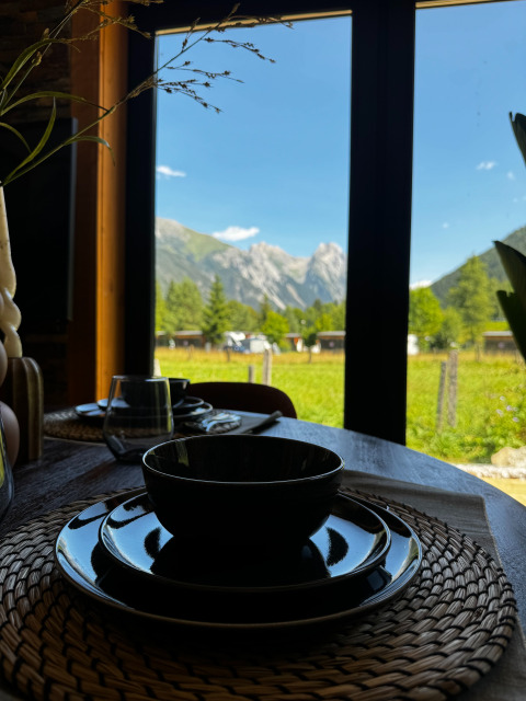 Table du petit-déjeuner devant une fenêtre avec vue sur les montagnes à Arlberg Cabin, Austriaparks Camping Arlberg, Autriche.