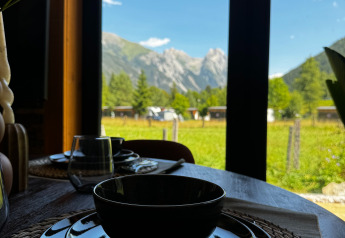 Mesa de desayuno junto a la ventana con vista a las montañas en Arlberg Cabin de Austriaparks Camping Arlberg, Austria.