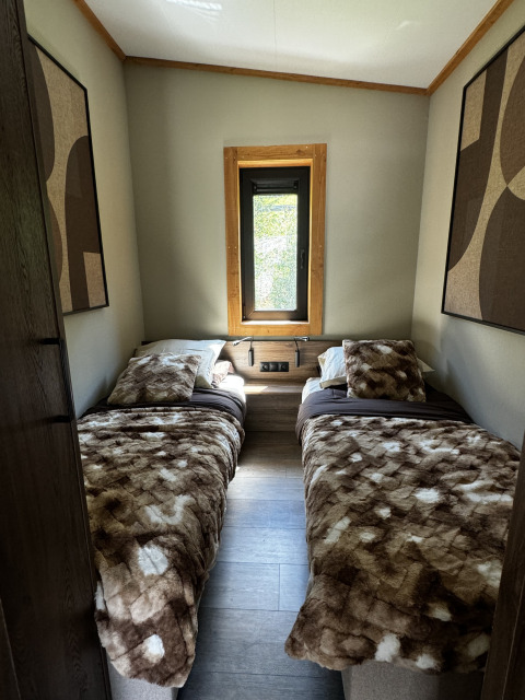 Chambre chaleureuse avec deux lits simples à l’Arlberg Cabin, Austriaparks Camping Arlberg en Autriche, vue fenêtre.