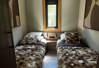 Chambre chaleureuse avec deux lits simples à l’Arlberg Cabin, Austriaparks Camping Arlberg en Autriche, vue fenêtre.
