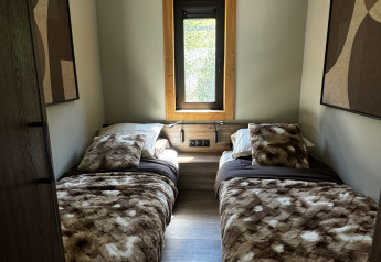 Dormitorio acogedor con dos camas individuales en Arlberg Cabin, Austriaparks Camping Arlberg, Austria, con ventana.