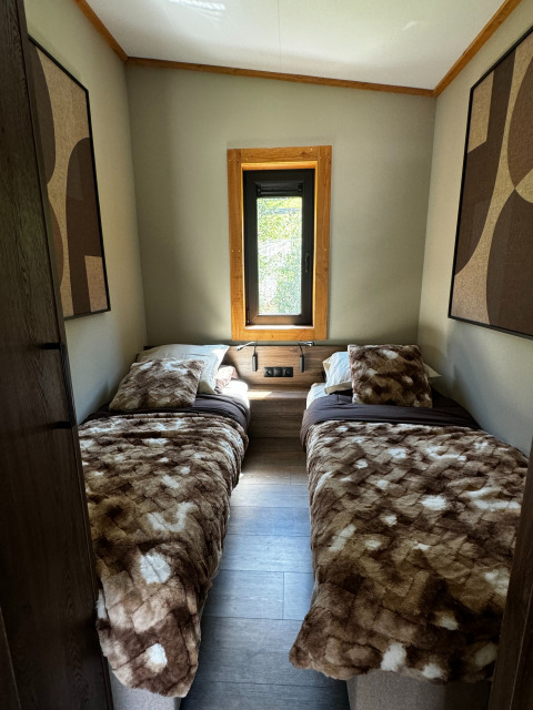 Chambre confortable avec deux lits simples, couvertures moelleuses et fenêtre à Arlberg Cabin, Austriaparks Camping Arlberg.