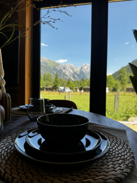 Table dressée avec vaisselle noire et vue sur la montagne par la fenêtre à Arlberg Cabin, Austriaparks Camping Arlberg.