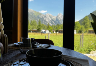 Table dressée avec vaisselle noire et vue sur la montagne par la fenêtre à Arlberg Cabin, Austriaparks Camping Arlberg.