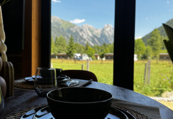 Mesa puesta con vajilla negra y vista a las montañas desde la ventana en Arlberg Cabin, Austriaparks Camping Arlberg.