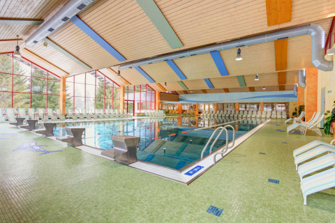 Piscine intérieure à Arlberg Cabin au Austriaparks Camping Arlberg, avec transats et grandes fenêtres.
