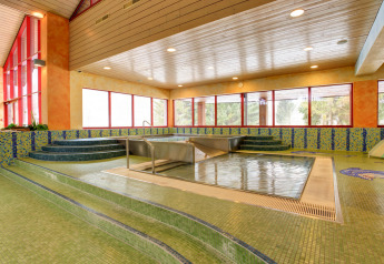 Piscina de spa interior con azulejos, escaleras y grandes ventanas en un alojamiento acogedor.