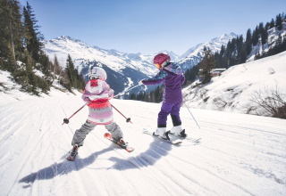 Deux enfants skient sur la neige près d’Arlberg Cabin, Austriaparks Camping Arlberg, Autriche, entourés de montagnes.