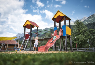 Twee kinderen spelen op een kleurrijke glijbaan bij een chalet met mooie bergen op de achtergrond.