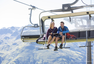 Deux personnes assises sur un télésiège admirant la vue sur les montagnes par temps ensoleillé et clair.