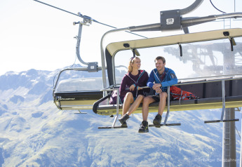 Deux personnes assises sur un télésiège admirant la vue sur les montagnes par temps ensoleillé et clair.