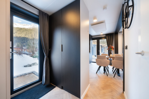 Moderne entree en eetruimte in een lodge met grote ramen en uitzicht op besneeuwde bergen.