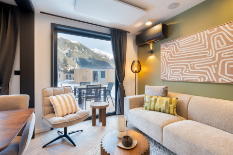 Moderne lodge woonkamer met grote ramen, uitzicht op bergen en stijlvolle inrichting tijdens de winter.