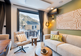 Moderne lodge woonkamer met grote ramen, uitzicht op bergen en stijlvolle inrichting tijdens de winter.