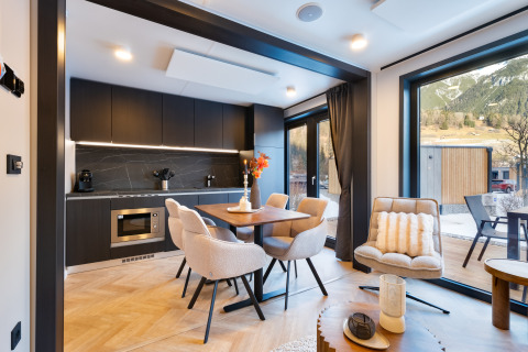 Moderne lodge met zwarte keuken, comfortabele eethoek en groot raam met uitzicht op de bergen.