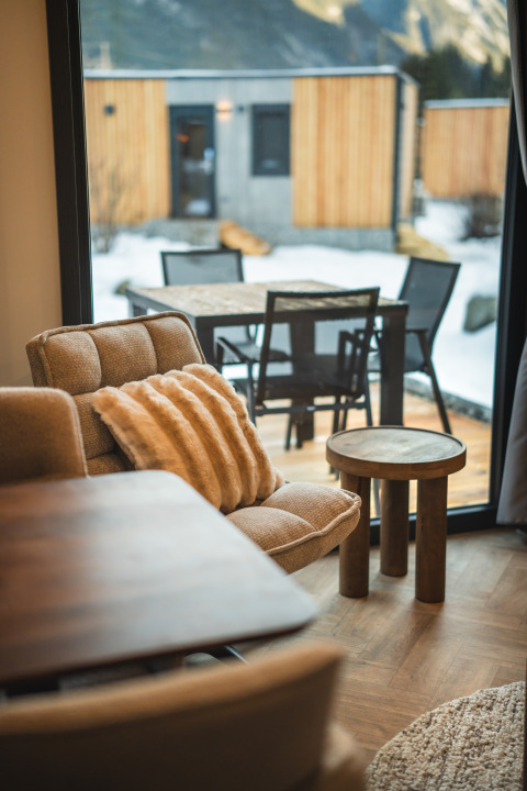 Gezellige zithoek met comfortabele stoel en tafel, uitzicht op besneeuwd terras bij lodge door het raam.