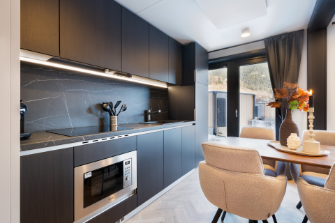 Moderne keuken en eethoek in een lodge met donkere kasten, eettafel en uitzicht naar buiten.