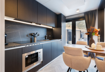 Cuisine et salle à manger modernes dans un lodge avec armoires foncées, table et vue extérieure.