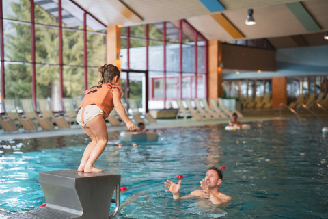 Een kind staat klaar om in een binnenzwembad te springen waar een volwassene in het water wacht bij een lodge.