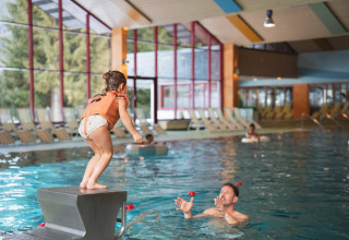 Et barn gør sig klar til at hoppe i en indendørs pool, hvor en voksen venter i vandet på et ferieanlæg.