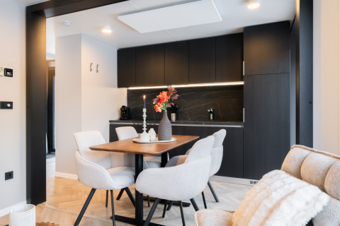 Moderne spiseområde ved lodge med sort køkken, lyse stole, træbord og elegant bordpynt.