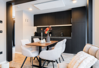 Moderne eetruimte in een lodge met zwarte keuken, lichte stoelen, houten tafel en stijlvolle decoratie.