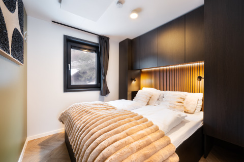 Modern lodge slaapkamer met zachte witte kussens, lichtbruine plaid, houten panelen en donkere kasten.