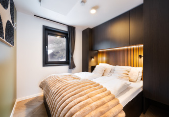 Chambre moderne en lodge avec oreillers blancs moelleux, plaid en fausse fourrure et panneaux en bois.