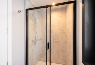 Moderne douche met glazen deuren en zwart frame in een lodge, licht en minimalistisch interieur.