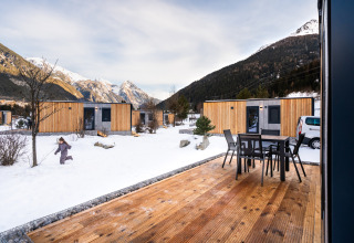 En lodge med træhytter i sneen, bjergudsigt, udendørs terrasse og et barn, der leger udenfor.