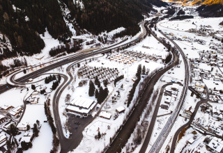 Luchtfoto van een lodge in de sneeuw met kronkelende wegen, verspreide huizen en besneeuwde bergen eromheen.